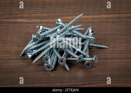 Metal screws in stack on a wooden background. Stock Photo