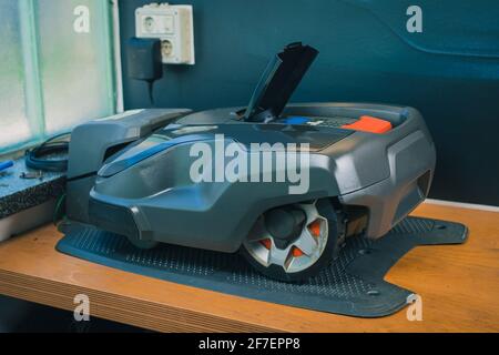 Modern robotic lawnmower being charged on a service stand in a garden charger Stock Photo