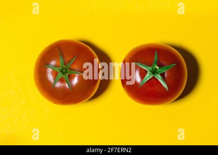 two tomatoes with green tails isolated on yellow background Stock Photo