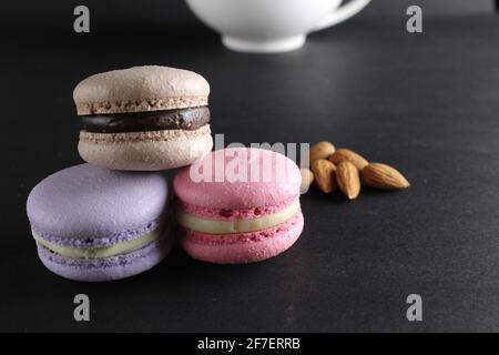 French dessert cuisine three macaroons lie pyramid to lies almonds and a cup of coffee in the background on a black background with a copyspace . Stock Photo