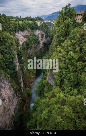Deep gorge valley with river of Adige in the bottom behind the dam of lake Giustina in Italy, close to the city of Cles. White train bridge visible in Stock Photo