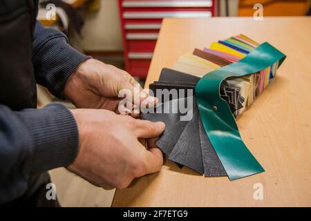 Hands are visible choosing different leather samples in a pack on a wooden table in a leatherman workshop. Upholstery shop choosing material. Stock Photo