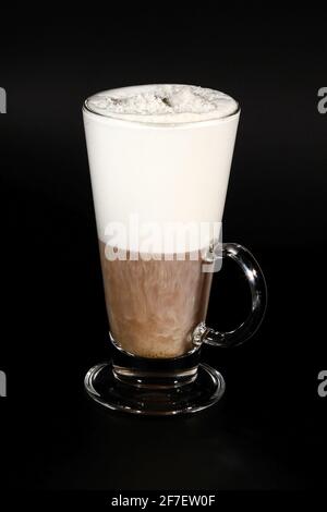 Hot chocolate or coffee beverage in glass cup with holder, isolated on black. Visible coconut crumbs, milk, whipped cream and other sweet ingredients. Stock Photo