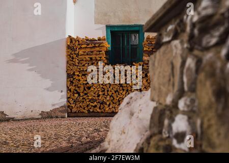 Stack or pile of fire wood lying next to a house rising up to the picturesque window frame in green color. Stock Photo