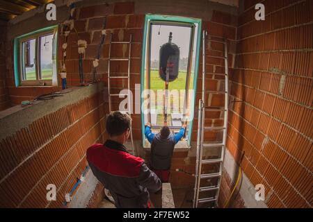 Two male workers installing a modern glass window into a new house being built using a hydraulic lift or crane mounted on a lorry. Modern installation Stock Photo