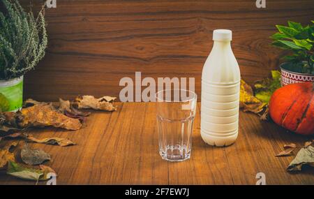 Fresh homemade natural youghurt drink in plastic container with a glass standing next to it. Beautiful autumn setting table for yoghurt drink. Fresh a Stock Photo