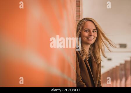 Cute fashionable young woman in a red brick hallway looking at a camera. Caucasian girl in a let's go mode, wanting to travel. Wanderlust hipster girl Stock Photo