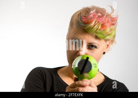 A young woman posing with a hairdryer as a gun. woman with yellow and pink funky haircut aiming with a hairdrier. Stock Photo