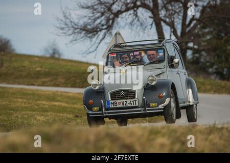 JANCE, SLOVENIA, 16.3.2019: A gray vintage Citroen 2CV car is driving from a curve with happy passengers inside on a country road. Stock Photo