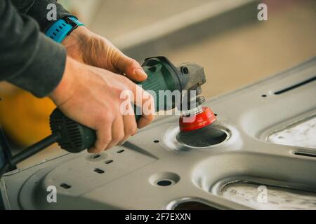 Young service man is using an angle grinder with a wire brush to clean the underside of an old vintage car about to be restored Stock Photo