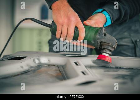 Young service man is using an angle grinder with a wire brush to clean the underside of an old vintage car about to be restored Stock Photo