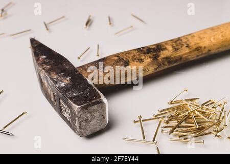 A used and worn european style hammer with a wooden handle and metal tip and some golden nails. Isolated on white reflective board. Golden nails are l Stock Photo