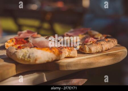 Two home made pizzas freshly baked and served on a wooden plate on a rustical table in a garden. Beautiful setting for a pizza. Stock Photo