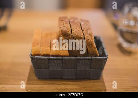 Slices of two different bread types in a grey woven basket on a wooden table. Fancy serving of bread slices  in shallow depth of field, focus on bread Stock Photo