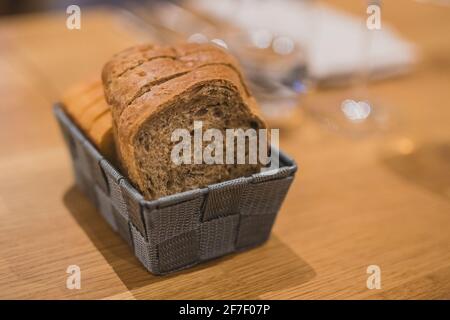 Slices of two different bread types in a grey woven basket on a wooden table. Fancy serving of bread slices  in shallow depth of field, focus on bread Stock Photo