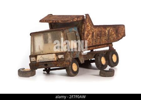 Side of an old, dirty and very rusty tin metal model toy of a dump truck in blue and grey color isolated on white background. Wheels have fallen off. Stock Photo