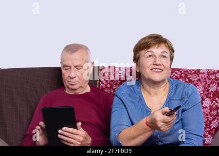 Senior married couple choosing movie on tv. Online broadcast from digital tablet on smart television. Elderly people at home relaxing on couch Stock Photo