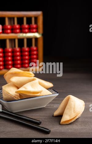 Close-up of chopsticks, fortune cookies on saucer, on dark wooden table with abacus, selective focus, black background, vertical Stock Photo