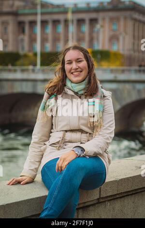 Young woman sitting in front of the Swedish parliament building in Stockholm on a dull autumn day. Stock Photo