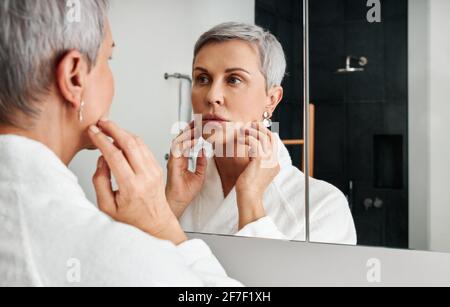 Mature woman with short grey hair touching her face Stock Photo