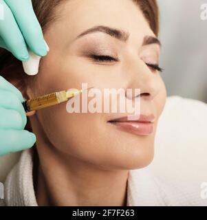 Adult beautiful woman during facial PRP therapy. Beautician doing blood plasma injection for patient face skin cell restoration, close-up Stock Photo