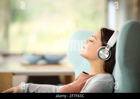 Side view portrait of a relaxed woman wearing wireless headphones listening to music on a wing chair