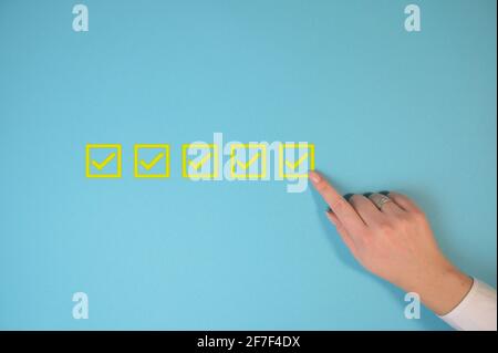 Yellow marking on checklist box isolated on blue background with copy space. Checklist concept. Businesswoman checking mark on the check boxes. Stock Photo