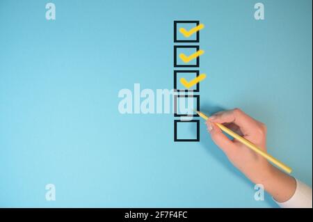 Yellow marking on checklist box isolated on blue background. Checklist concept. Hand holding a pencil and checklist isolated on pastel blue Stock Photo
