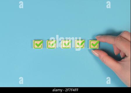 Checklist concept, check mark on wooden blocks on pastel blue background with copy space. Hand holding wooden blocks with check marks. Stock Photo