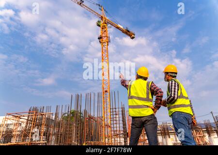 Construction engineers and  architect supervising progress of building construction project stand on new concrete floor top roof and crane background Stock Photo