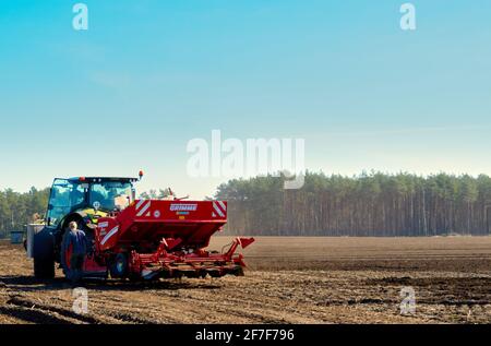 Gifhorn Germany, March 30., 2021: Tractor plowing a potato field in front of a pine forest Stock Photo