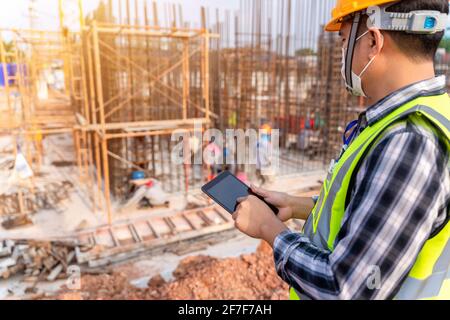Construction civil engineer or architect with hardhat on construction site checking schedule and building foundations project on tablet computer at co Stock Photo