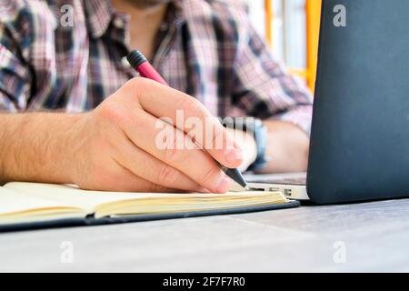 Close-up of a man's hands writing in a notebook in front of the computer. E-learning from home concept. Stock Photo