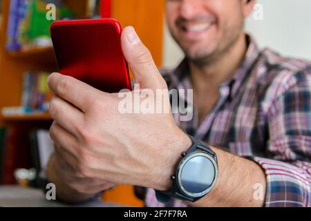 Wide shot of a man in front of a smartphone, making a video conference and smiling. Concept of teleworking from home. Concept of telecommuting from ho Stock Photo