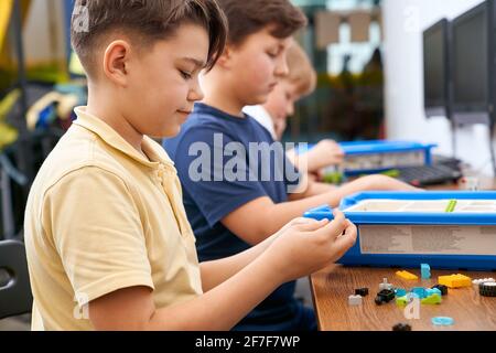 Interesting building kit for kids on table with computers. Side view of boys creating toys. Science engineering. Nice interested friends chatting and working on project together. Stock Photo