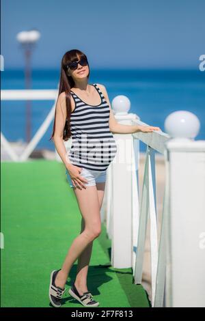 Beautiful pregnant woman relaxing outside near the sea. Stock Photo