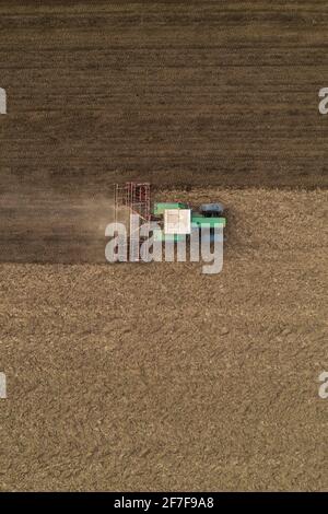 Aerial view of agricultural tractor tilling and harrowing ploughed field, directly above drone pov image of machinery working on farmland Stock Photo