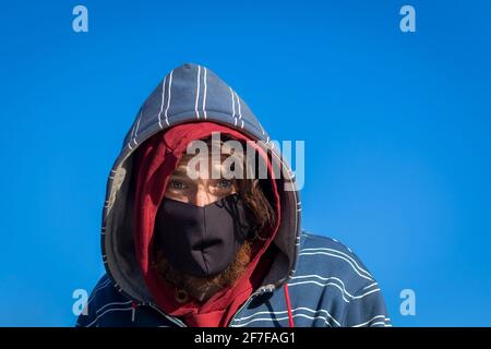 Ginger bearded Irish man with a face mask and hoods in front of a blue sky Stock Photo
