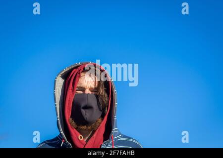 Ginger bearded Irish man with a face mask and hoods in front of a blue sky Stock Photo