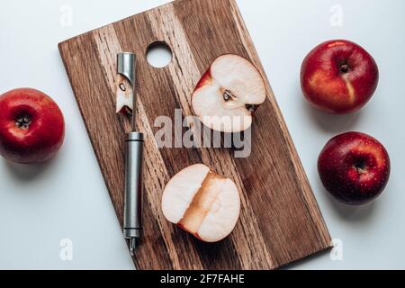 Halves of a red apple on a wooden board with a knife on a kitchen table Stock Photo
