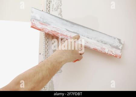 Builder in protective mask using a trowel to add plaster. Plastering wall with putty-knife, close up image. Fixing wall surface and preparation for pa Stock Photo