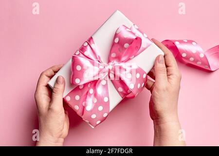 Gift box with big bow in female hands on pink background, top view. White gift box with long pink ribbon, flat lay Stock Photo