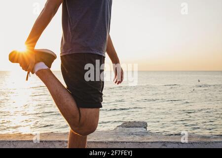 Man stretching at sunrise near the sea with the sun in the background and lens flare. Stock Photo