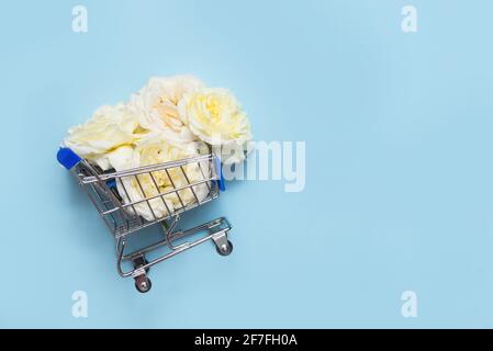 shopping cart with white roses on blue background with copy space