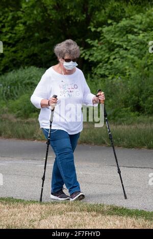 An older woman out for an exercise walk in Little Bay Park in Whitestone, Queens, New York using walking sticks and listening to music. Stock Photo