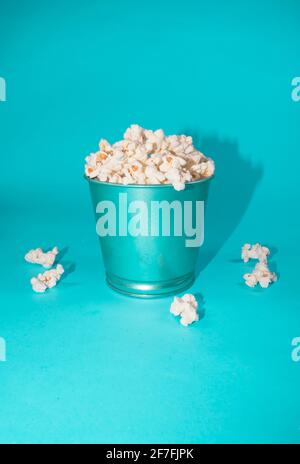 Bowl of pop corns with blue bowl and blue background. Spilled pop corns laying around. Isolated close up. Stock Photo