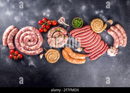 Set of different raw beef, pork and chicken meat sausages on cooking table with spices, sauces and vegetables for grilling. Bbq party concept, black b Stock Photo