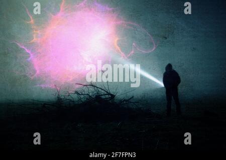 A science fiction concept. Of a man with a torch looking at an alien cloud of energy in the sky, in a field on a misty winters night. With a grunge, v Stock Photo