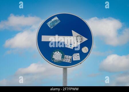 arrow in circle blue road sign against a blue sky, turn right. Sign covered in stickers. Stock Photo
