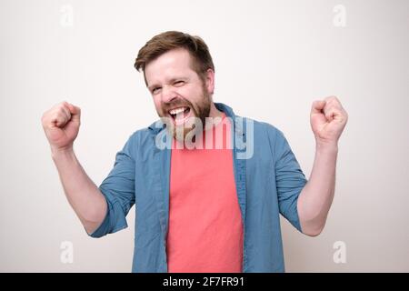 Joyful man makes a winner gesture, he is happy and emotionally shouts. Positive emotions. White background. Stock Photo